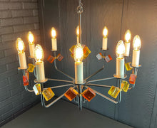Load image into Gallery viewer, Chandelier with colorful glass shades against a brick wall.