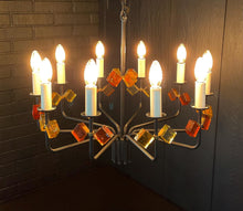 Load image into Gallery viewer, Decorative chandelier with colorful glass shades against a brick wall.