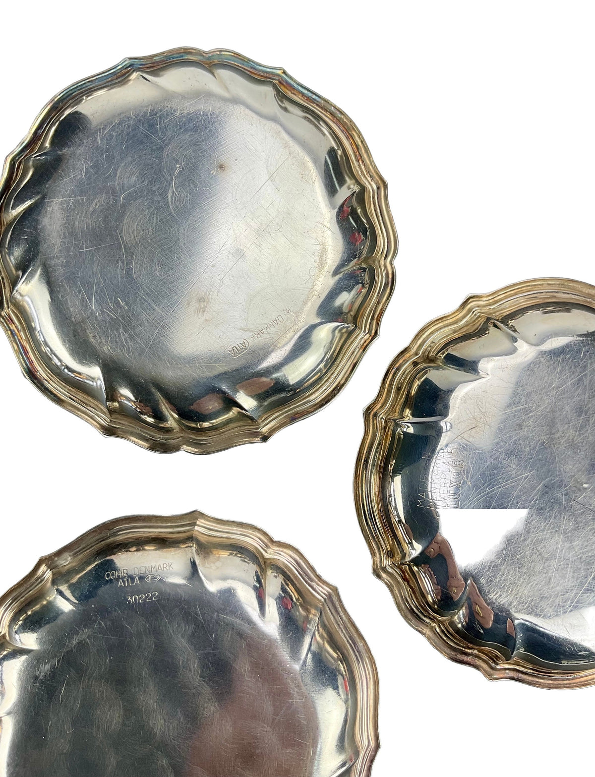 Three silver coasters with scalloped edges on a white background