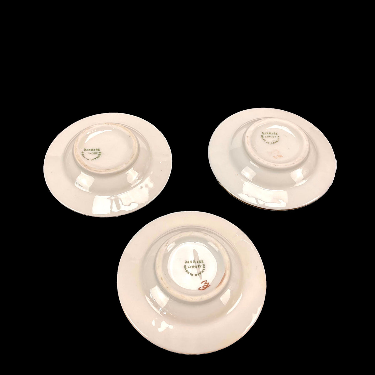Three white ceramic plates with visible branding on a black background