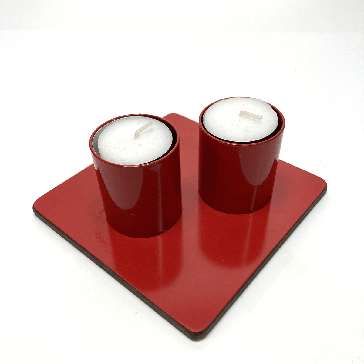 Two red candle holders with white candles on a red square base against a white background