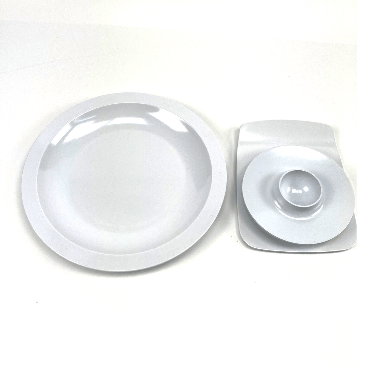 Round white melamine egg cup, buttering board, and a plate with a central indentation on a white background