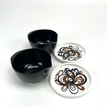Load image into Gallery viewer, Two black bowls and two white coasters with brown floral patterns on a white background
