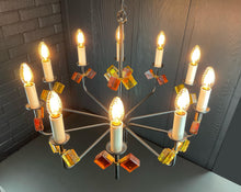 Load image into Gallery viewer, Chandelier with colorful glass shades against a brick wall.
