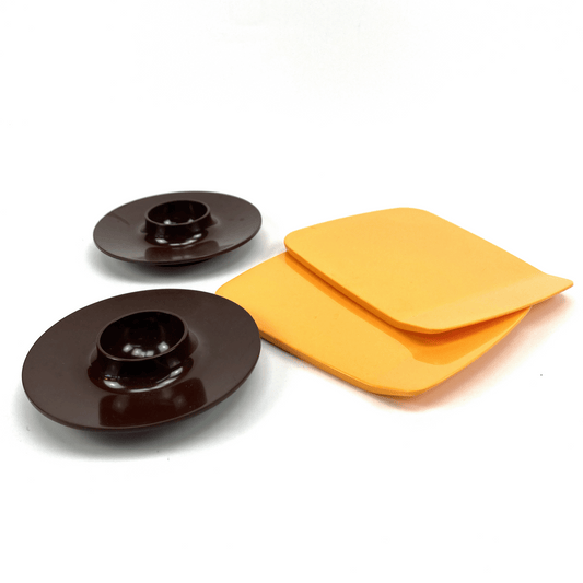 Two circular brown egg cups and two yellow square buttering boards on a white background