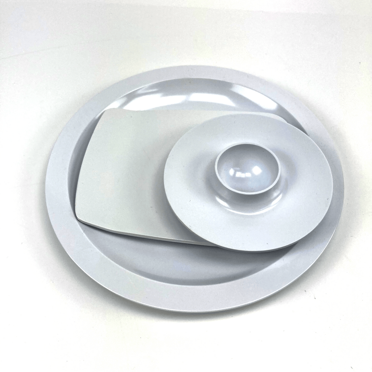 Round white melamine egg cup, buttering board, and a plate with a central indentation on a white background